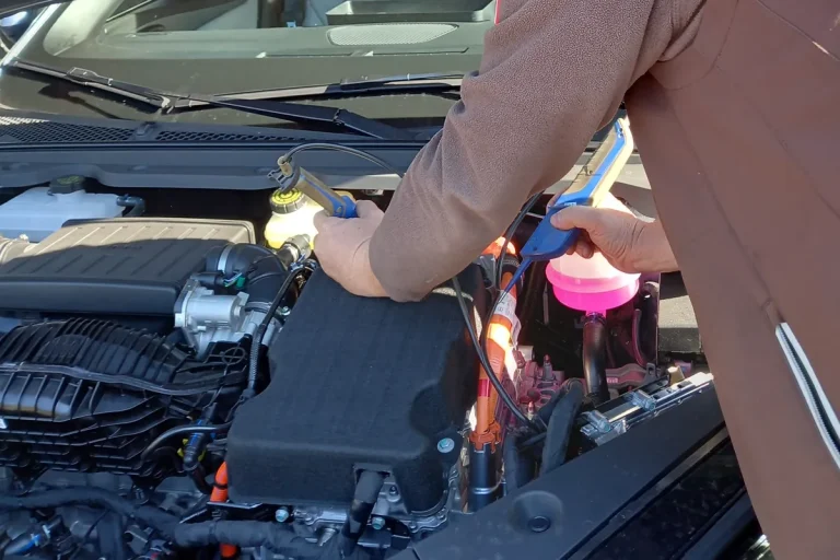 Mitarbeiter arbeitet im Motorraum eines Hybridautos mit orangen Hochvoltkabeln