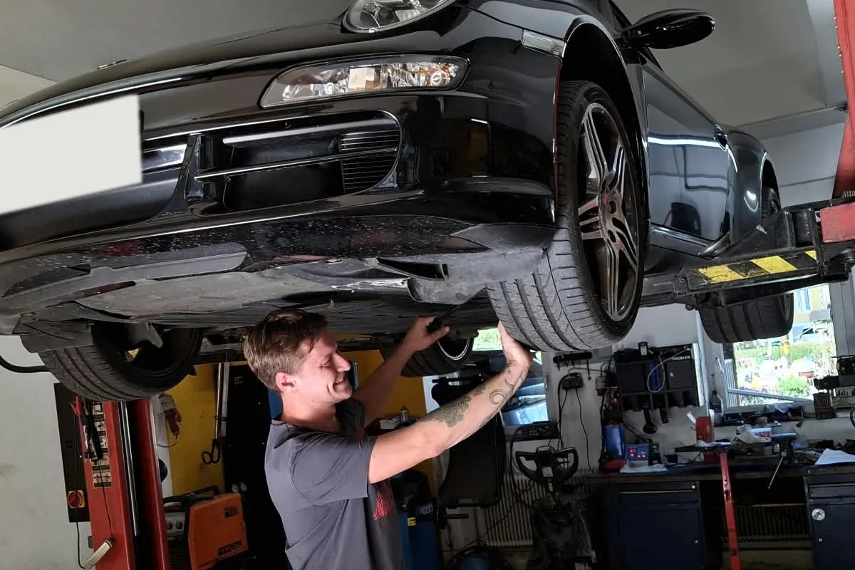 Mitarbeiter am Rad eines angehobenen Autos in der Werkstatt in Ligist